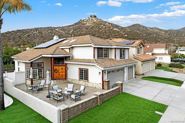 rear view of property featuring a patio area, a mountain view, solar panels, a yard, and a garage