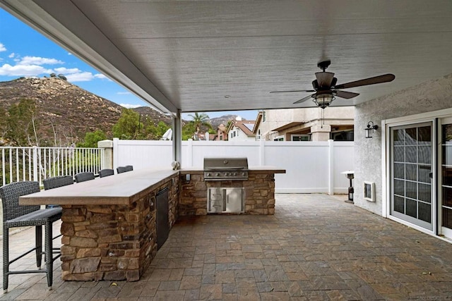 view of patio / terrace featuring a bar, an outdoor kitchen, ceiling fan, a mountain view, and grilling area