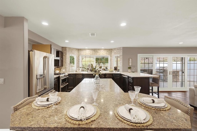 kitchen featuring a kitchen island, high end appliances, light stone countertops, a kitchen breakfast bar, and french doors