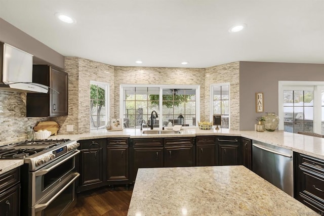 kitchen featuring a healthy amount of sunlight, stainless steel appliances, wall chimney exhaust hood, and sink