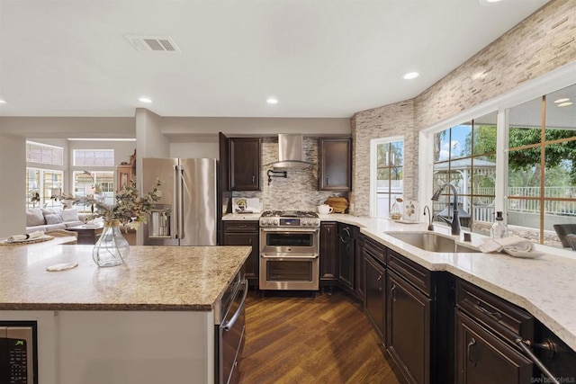 kitchen with sink, dark hardwood / wood-style flooring, dark brown cabinetry, stainless steel appliances, and wall chimney exhaust hood