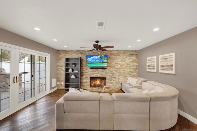 living room featuring dark wood-type flooring, ceiling fan, french doors, and a stone fireplace