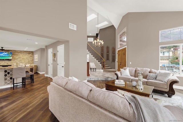 living room featuring dark wood-type flooring, ceiling fan with notable chandelier, and high vaulted ceiling