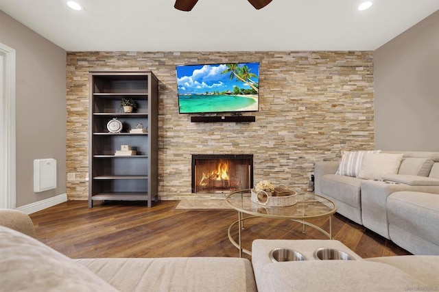 living room with hardwood / wood-style flooring, ceiling fan, built in shelves, and a stone fireplace