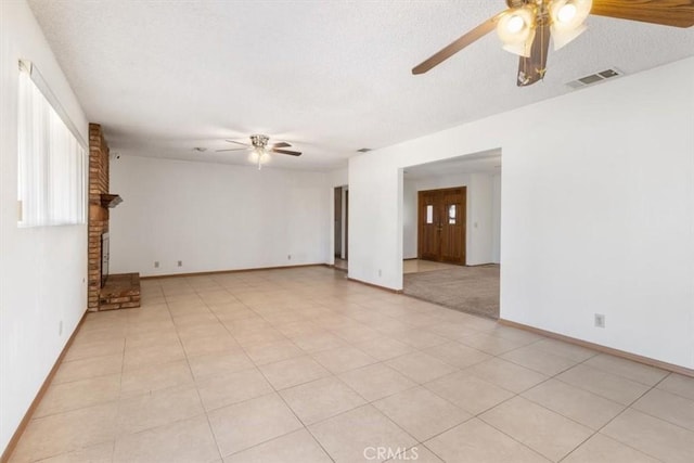 empty room featuring a fireplace, visible vents, ceiling fan, a textured ceiling, and baseboards