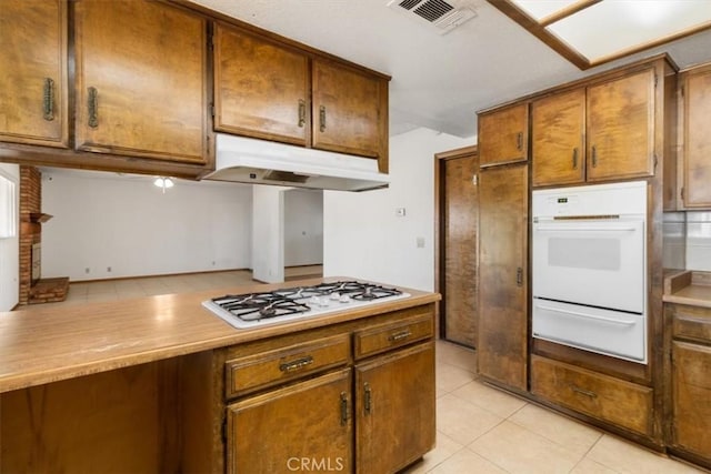 kitchen featuring visible vents, light countertops, light tile patterned flooring, white appliances, and under cabinet range hood