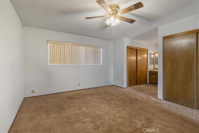 unfurnished bedroom with light carpet, a textured ceiling, a ceiling fan, and multiple closets