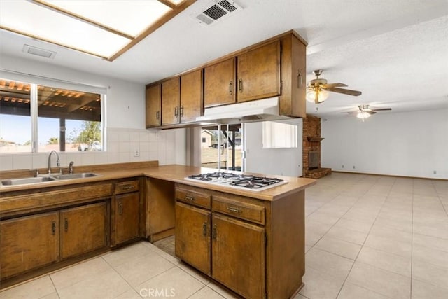 kitchen featuring a peninsula, light countertops, under cabinet range hood, white gas cooktop, and a sink