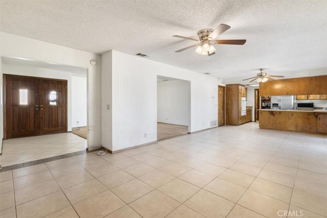 unfurnished living room featuring a textured ceiling, ceiling fan, light tile patterned floors, visible vents, and baseboards