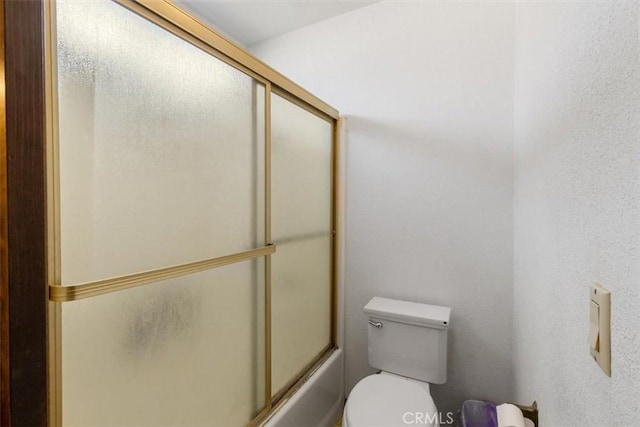 bathroom with toilet and shower / bath combination with glass door