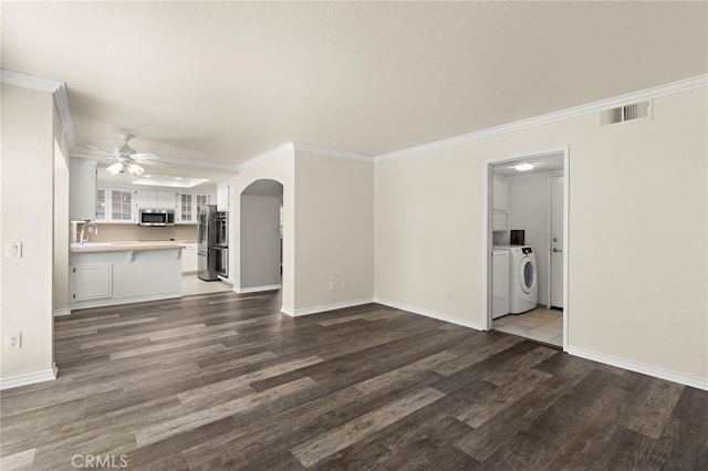 unfurnished living room featuring ceiling fan, dark wood-type flooring, ornamental molding, and washing machine and clothes dryer