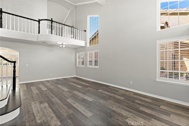 unfurnished living room featuring dark wood-type flooring and a towering ceiling