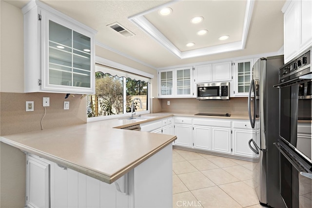 kitchen featuring white cabinets, stainless steel appliances, sink, kitchen peninsula, and a tray ceiling