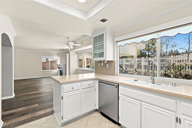 kitchen with light tile patterned floors, kitchen peninsula, stainless steel dishwasher, white cabinets, and sink