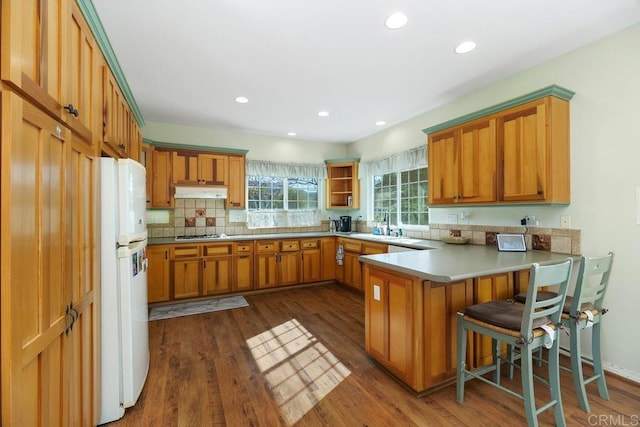 kitchen with dark hardwood / wood-style floors, white refrigerator, kitchen peninsula, tasteful backsplash, and stainless steel gas stovetop