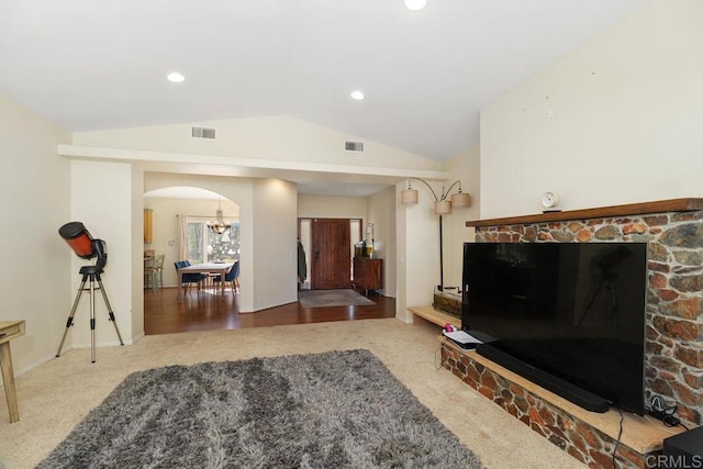 living room featuring lofted ceiling, carpet flooring, and a stone fireplace