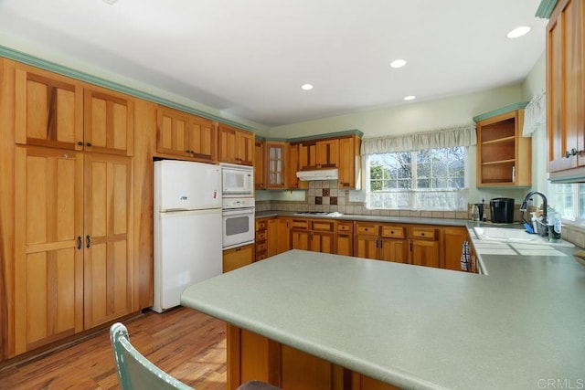 kitchen featuring white appliances, light wood-type flooring, decorative backsplash, sink, and kitchen peninsula