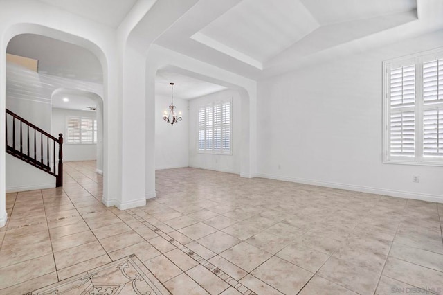 tiled empty room featuring a notable chandelier, a raised ceiling, and a wealth of natural light