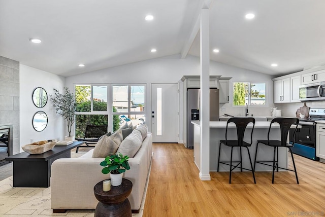 living room with a tile fireplace, light hardwood / wood-style flooring, a healthy amount of sunlight, and vaulted ceiling with beams