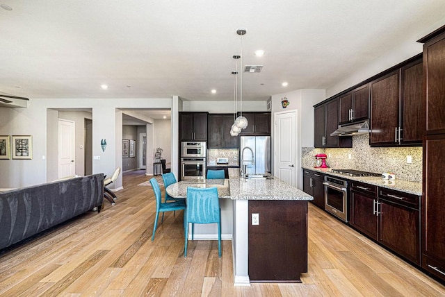 kitchen with a center island with sink, tasteful backsplash, pendant lighting, light hardwood / wood-style flooring, and sink