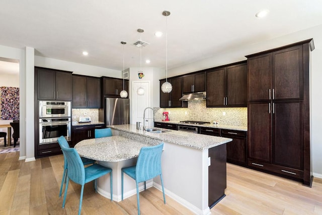 kitchen with pendant lighting, a center island with sink, sink, stainless steel appliances, and light stone counters