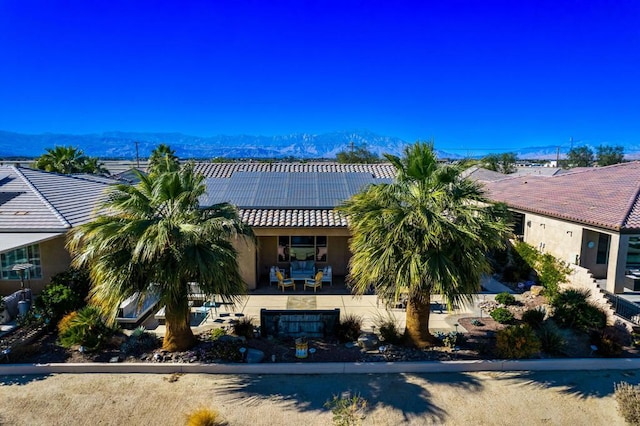 view of front facade featuring a mountain view, solar panels, and a patio