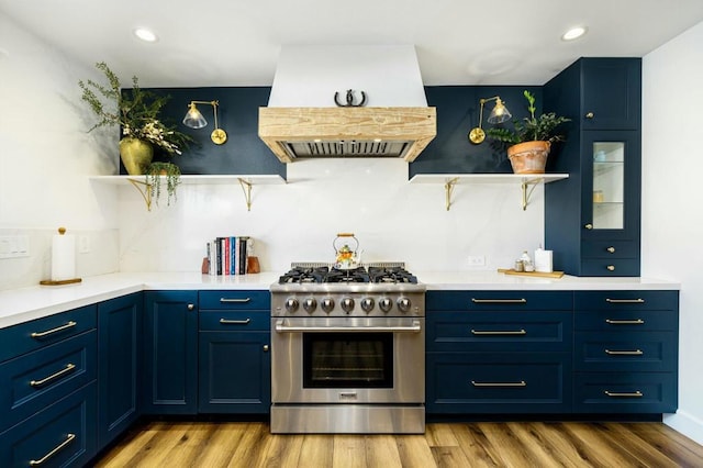 kitchen featuring premium range hood, blue cabinetry, high end stove, and light hardwood / wood-style flooring