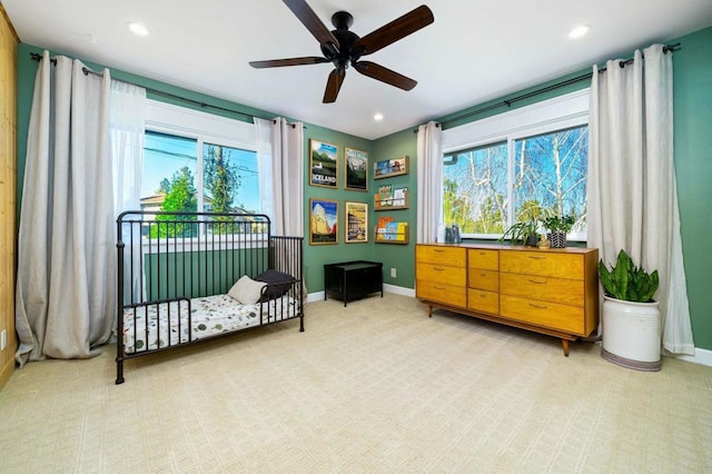 bedroom featuring a nursery area, light carpet, and ceiling fan