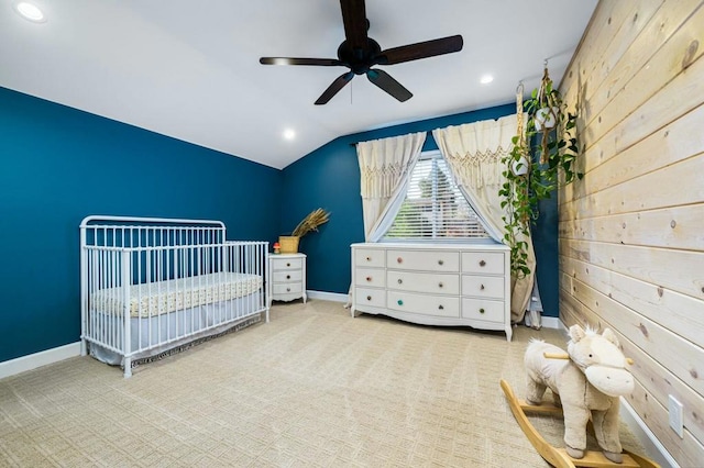 carpeted bedroom featuring a nursery area, wood walls, ceiling fan, and vaulted ceiling