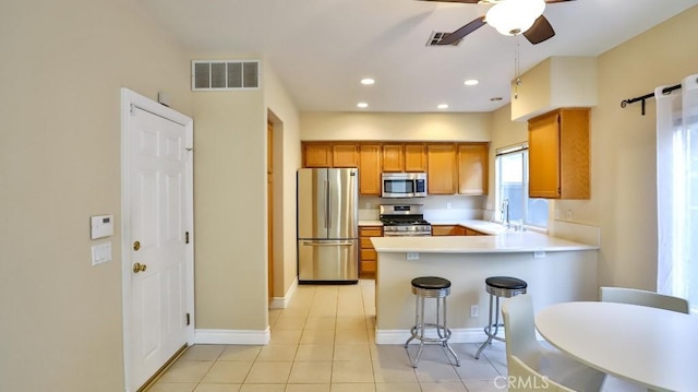 kitchen featuring kitchen peninsula, a breakfast bar area, appliances with stainless steel finishes, ceiling fan, and sink