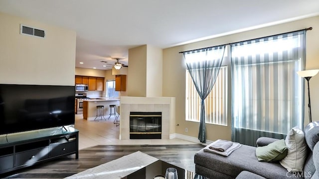 living room with ceiling fan, dark hardwood / wood-style floors, and a tiled fireplace