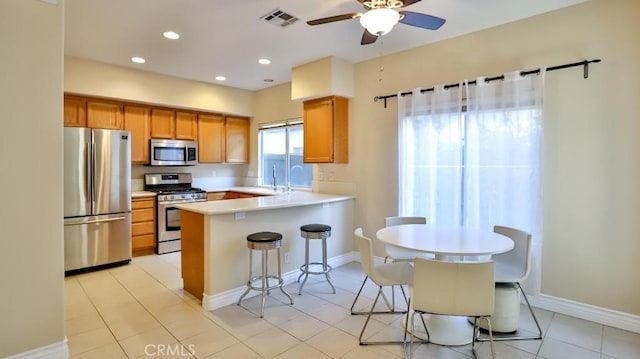 kitchen with ceiling fan, kitchen peninsula, appliances with stainless steel finishes, a breakfast bar area, and light tile patterned floors