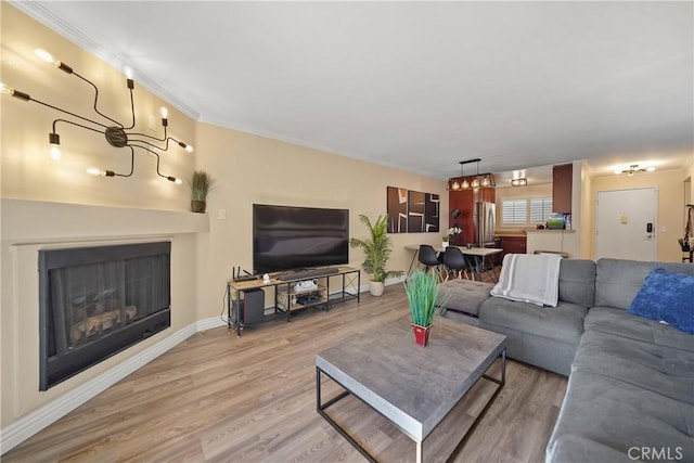 living room featuring a fireplace, light wood-style floors, an inviting chandelier, and ornamental molding