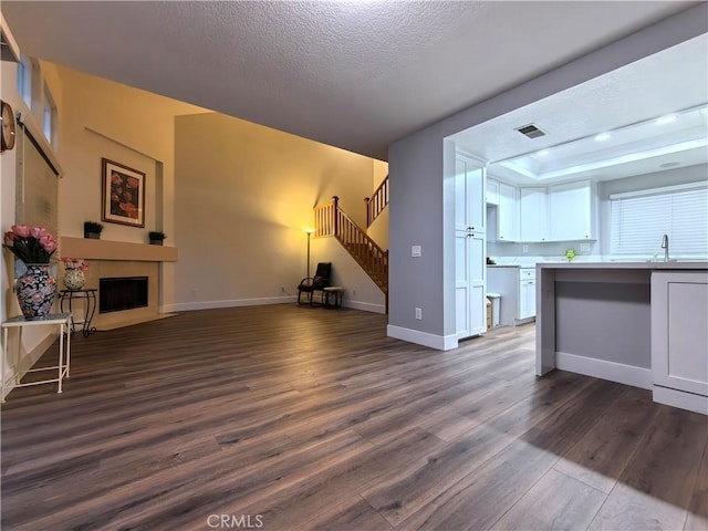 unfurnished living room with sink, dark hardwood / wood-style flooring, a textured ceiling, and a tray ceiling