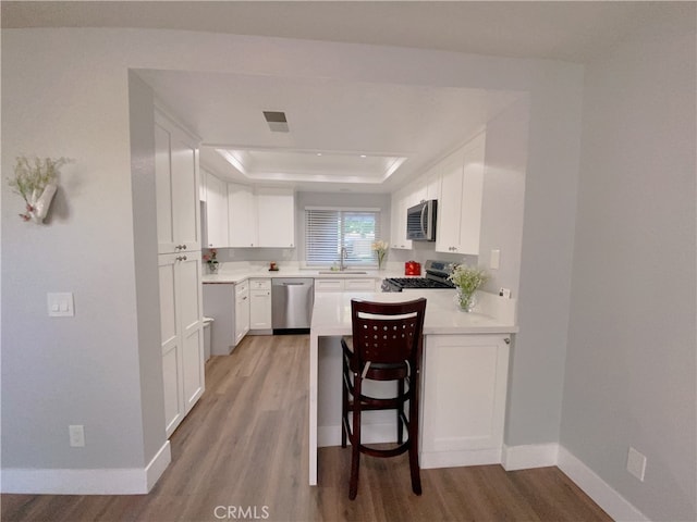1911 E Calico Dr, West Covina, CA 91791 - kitchen with appliances with stainless steel finishes, a raised ceiling, light wood-type flooring, a peninsula, and baseboards