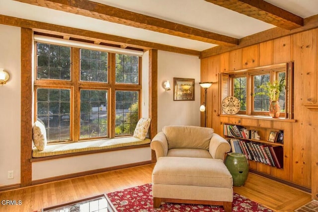 living area with wood walls, hardwood / wood-style floors, and beam ceiling