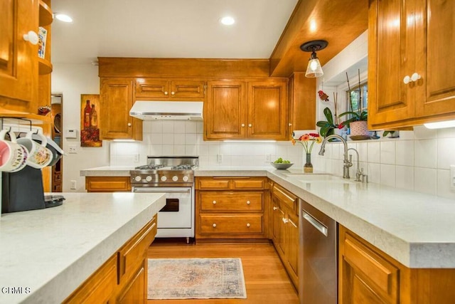 kitchen with pendant lighting, exhaust hood, backsplash, appliances with stainless steel finishes, and sink