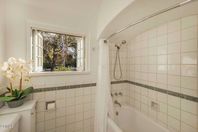 bathroom with tile walls, a healthy amount of sunlight, vaulted ceiling, and shower / bath combo