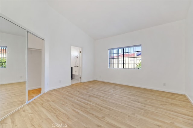 unfurnished bedroom featuring ensuite bath, high vaulted ceiling, a closet, and light hardwood / wood-style flooring