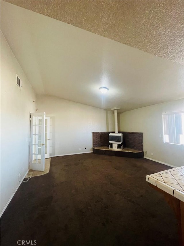 unfurnished living room with vaulted ceiling, a wood stove, a textured ceiling, and carpet flooring