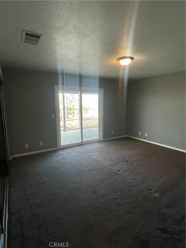 unfurnished room with a textured ceiling and dark colored carpet