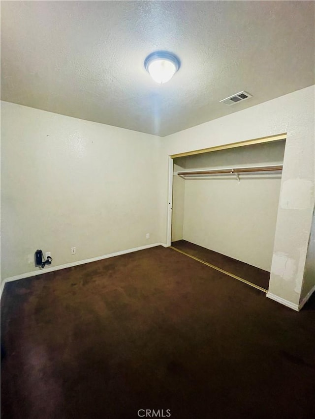 unfurnished bedroom featuring a textured ceiling, a closet, and dark colored carpet