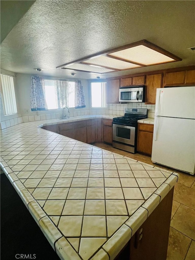 kitchen featuring sink, tasteful backsplash, a textured ceiling, appliances with stainless steel finishes, and tile counters