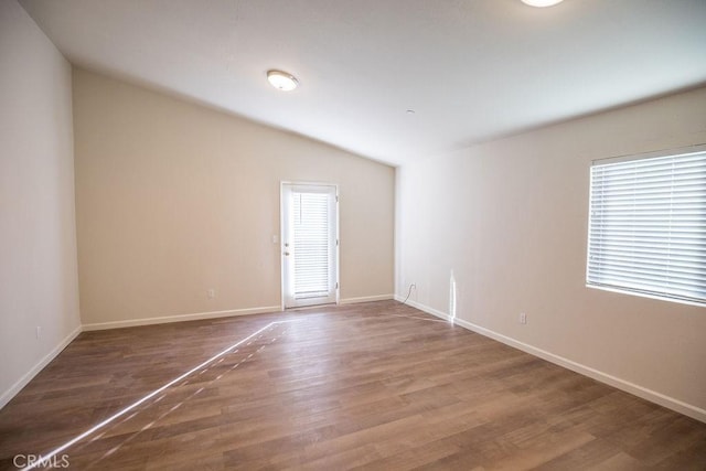 spare room featuring lofted ceiling, a healthy amount of sunlight, and hardwood / wood-style floors