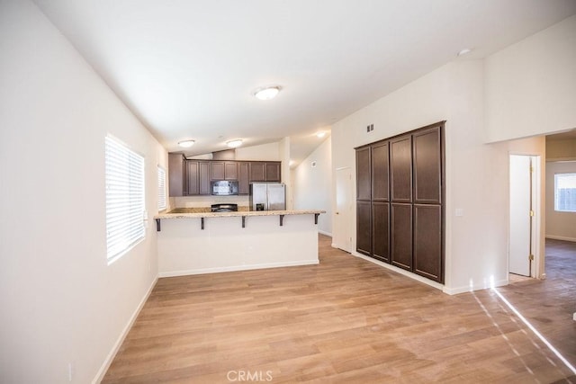 kitchen featuring kitchen peninsula, stainless steel refrigerator with ice dispenser, light wood-type flooring, a kitchen breakfast bar, and dark brown cabinets