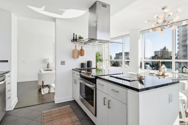 kitchen with an inviting chandelier, island exhaust hood, stainless steel appliances, dark tile patterned flooring, and white cabinets