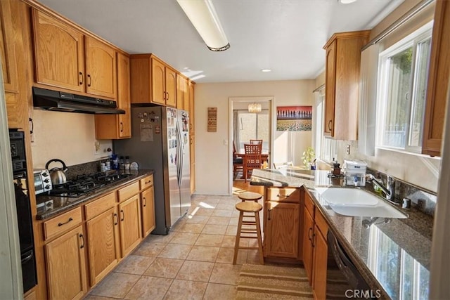 kitchen with sink, light tile patterned floors, dark stone countertops, a kitchen breakfast bar, and black appliances