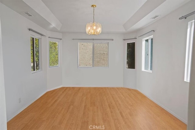 spare room featuring a raised ceiling, light hardwood / wood-style flooring, and a notable chandelier