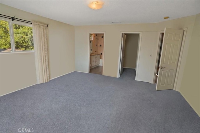 unfurnished bedroom featuring connected bathroom and dark carpet