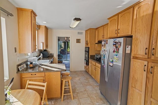 kitchen featuring stainless steel refrigerator, dark stone counters, a kitchen bar, and sink